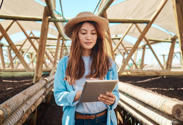 a young woman using a digital tablet while working on a farm. - Фото, изображение