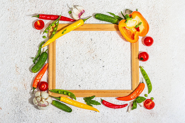 Assorted fresh vegetables and spices around wooden frame. Ripe yellow pepper, tomato, pea, cucumber, garlic, colored chilies. Ingredients for cooking healthy food, putty background, top view - Photo, image