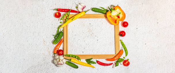 Assorted fresh vegetables and spices around wooden frame. Ripe yellow pepper, tomato, pea, cucumber, garlic, colored chilies. Ingredients for cooking healthy food, putty background, banner format - Foto, Bild