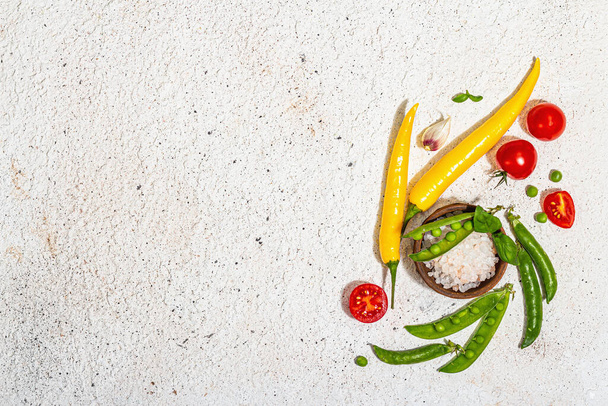 Assorted fresh vegetables and spices on light plaster background. Ripe yellow pepper, tomato, pea, cucumber, garlic, colored chilies. Ingredients for cooking healthy food, top view - 写真・画像