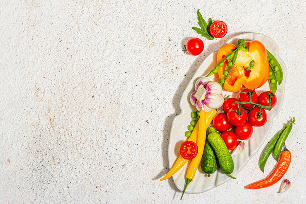 Harvest fresh vegetables on a serving plate. Vegan food concept, trendy hard light, dark shadow. Light plaster background, top view - Фото, изображение