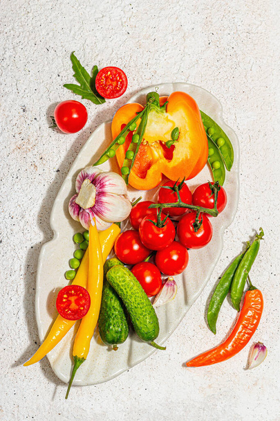 Harvest fresh vegetables on a serving plate. Vegan food concept, trendy hard light, dark shadow. Light plaster background, top view - 写真・画像