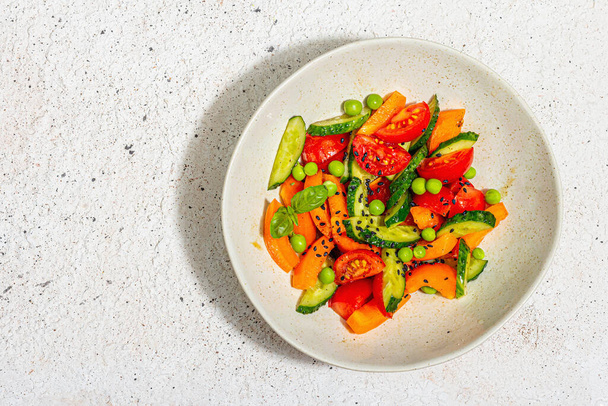 Summer vegetables salad in a modern bowl. Bright vegan food, trendy hard light, dark shadow. Light plaster background, top view - Foto, imagen