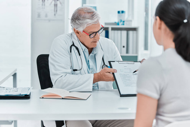 I need you to fill this out. a mature doctor sitting with his patient and showing a medical chart during a consultation in his clinic - Foto, Imagem