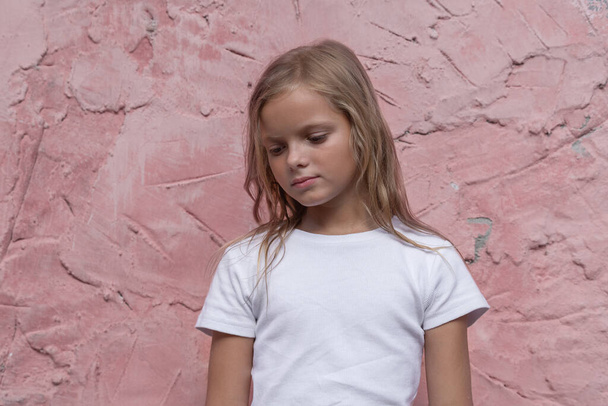 A preteen girl with blond hair poses for the camera against a pink wall. - Foto, Bild