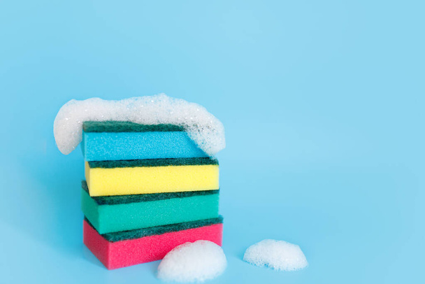 Multicolored sponges for cleaning on a blue background. Space for text - 写真・画像