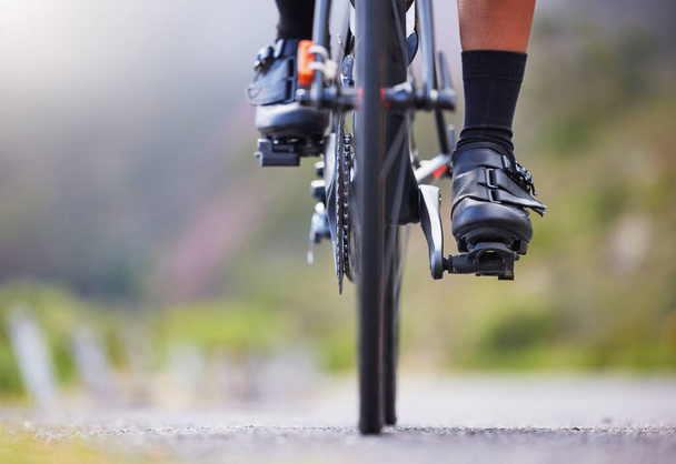 Closeup of one woman cycling outside. Sporty fit female athlete with her feet on bicycle pedals while riding a bike on a road for exercise. Endurance and cardio during a workout and training. - Fotoğraf, Görsel