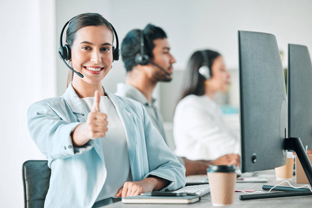Portrait of a young call centre agent showing thumbs up while working in an office with her colleagues in the background. - Фото, зображення