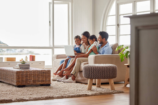 Молода щаслива сім'я проводить якісний час разом на дивані і використовує ноутбук для перегляду своїх улюблених шоу вдома
. - Фото, зображення