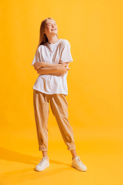 Happy smiling model. One young beautiful girl, student in casual style outfit isolated on bright yellow background. Concept of beauty, art, fashion, youth, healthy lifestyle. Copyspace for ad, text - 写真・画像