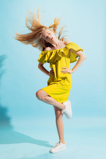 Dancing. Studio shot of young beautiful blonde in summer yellow dress isolated on light blue background. Concept of beauty, art, fashion, youth, healthy lifestyle. Copyspace for ad, text, sales offer. - Fotoğraf, Görsel