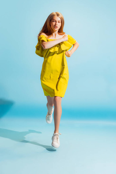 Running. Studio shot of young beautiful blonde in summer yellow dress isolated on light blue background. Concept of beauty, art, fashion, youth, healthy lifestyle. Copyspace for ads, text, sales offer - 写真・画像