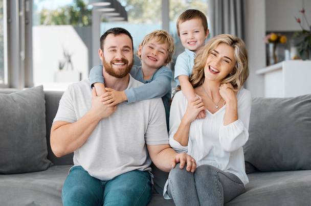 Portrait of smiling caucasian family relaxing together on a sofa at home. Carefree playful little sons hugging arms around loving parents. Happy kids bonding and spending quality time with mom and dad - Photo, Image