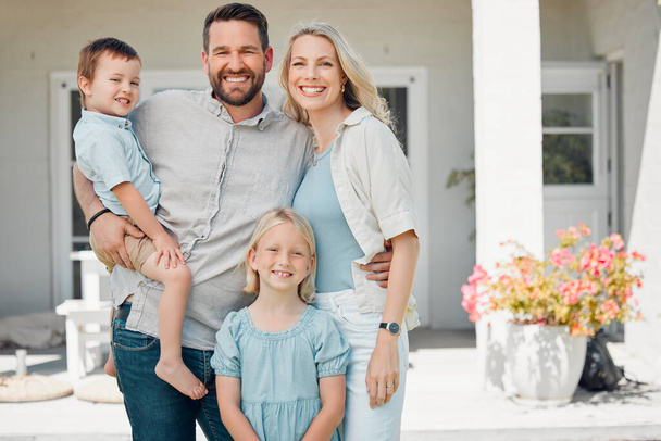 Portrait of happy parents standing with their children in front of their new property. Smiling caucasian couple bonding with their adorable son and daughter in front of their new home. - Fotó, kép