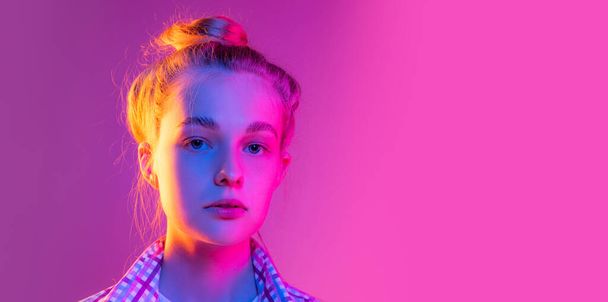 Closeup face of young calm girl, student looking at camera isolated on magenta color background in neon light. Concept of beauty, art, fashion, youth, sales and ad, education, studying. - Foto, imagen