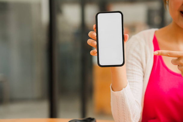 mooi aziatisch meisje een schattig meisje toont een grote smartphone met een wit leeg scherm in haar hand. Zittend aan tafel met een tablet - Foto, afbeelding
