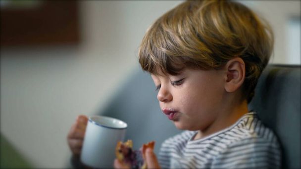 Toddler eating bread with jelly and drinking from mug in breakfast - Foto, immagini