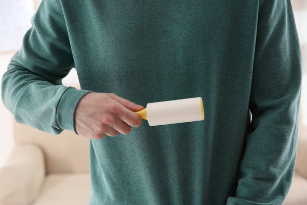 Man cleaning green sweatshirt with lint roller on light background, closeup - 写真・画像