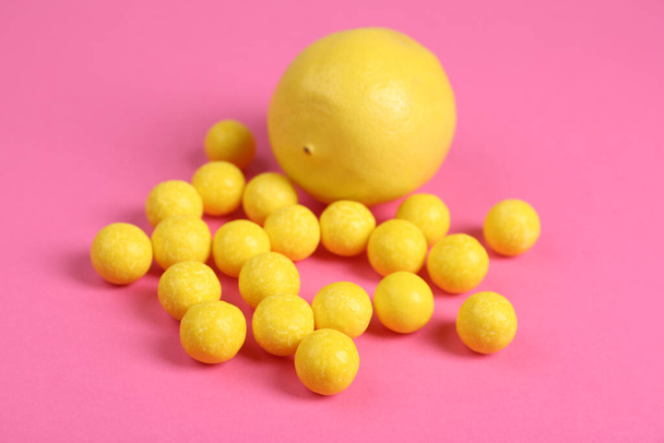 Whole fresh lemon and yellow candies on pink background - Fotó, kép