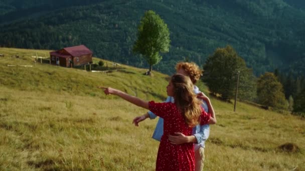 Travel couple look landscape view on mountains nature. Joyful family spend summer holiday. Positive millennials point finger green hill. Smiling lovers hug embrace on outdoors activity. Love concept. - Filmati, video