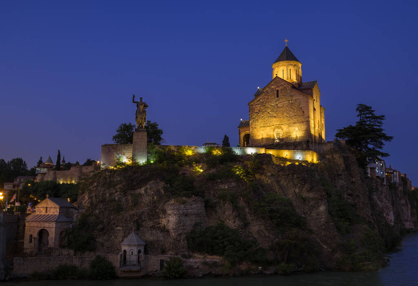 Evening Tbilisi (old Tiflis) Statue of King Vakhtang next to the Metekhi Church on the rocky bank of the river Kura litted by night city light. - Foto, immagini