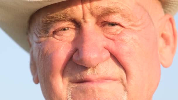 Mavi gökyüzünde kırışıklıkları olan yorgun yaşlı bir büyükbabanın portresi. Şapkalı bir emekli.. - Video, Çekim
