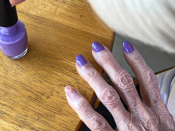 Senior woman polishing her nails with purple nail polish and giving herself a manicure. - Valokuva, kuva