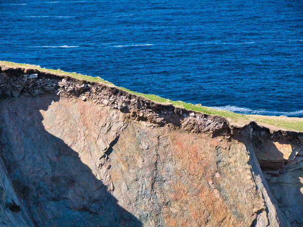 Eroding soil, subsoil and bedrock shown on sheer cliffs near Uyea in Northmavine, Shetland, UK. Taken on a sunny day with the sea in the background. - Φωτογραφία, εικόνα