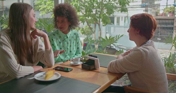 Gelukkige diverse vrouwelijke vrienden die samen rondhangen in de coffeeshop. Drie jonge vrouwen praten in café glimlachend en lachend - Foto, afbeelding