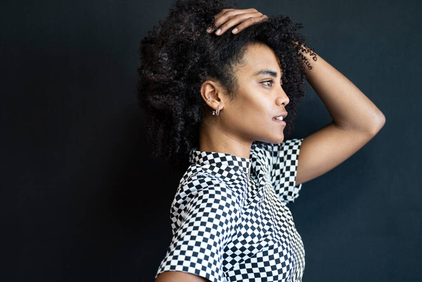 Portrait of young woman with afro hairstyle on the black background. Profile. Natural beautiful girl with curly hair. Fashionable female model - Foto, Imagem