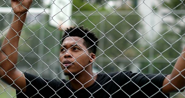 Pensive young black man leaning on metal fence. Contemplative mixed race person - Photo, Image