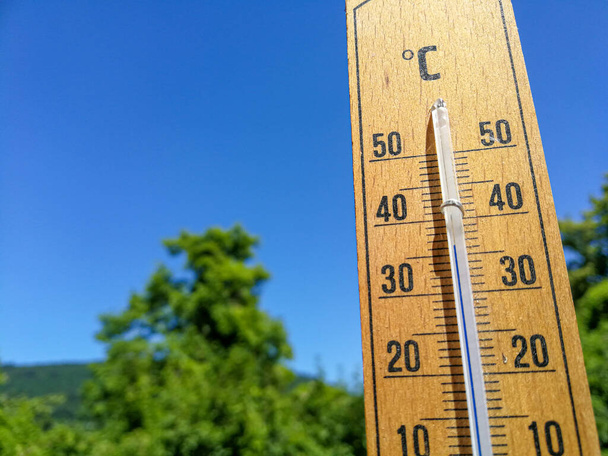 Деталь термометра показывает высокую температуру более 35 летом против деревьев и безоблачного неба с акцентом на термометр - Фото, изображение