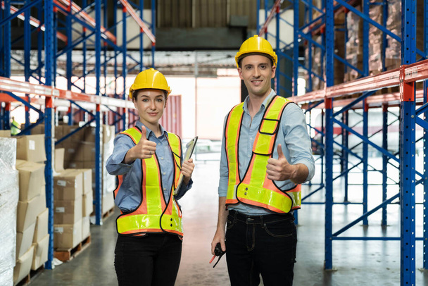 Мужчина и женщина в жёлтом шлеме и мужчина на складе показывают большой палец вместе для успешной работы со счастливым лицом. Командный дух, работающий вместе на складе для завершения инвентаризации баланса, - Фото, изображение