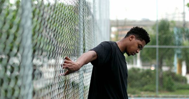 Μαύρος στο γήπεδο του μπάσκετ με μεταλλικό φράχτη να ποζάρει. - Φωτογραφία, εικόνα