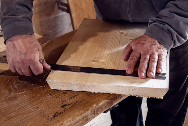 falegname maschile segna una tavola di legno con un righello e una matita nel suo laboratorio di casa. lavorazione del legno. - Foto, immagini