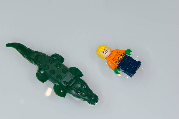Bauru, Brazil. 7, June, 2022: Top view of Lego minifigure of Aquaman angry swimming belly up with big fierce crocodile in his pool on white background. Space area. Minifigure are made by Lego Group - Foto, immagini