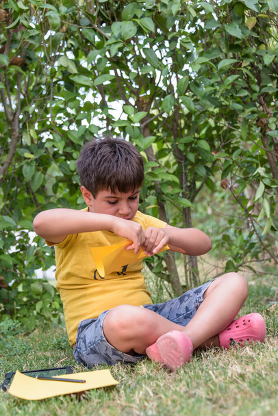 A srác, aki papírrepülőt játszik, elfordítja a tekintetét. Portré egy vidám kaukázusi fiú játszik a tavaszi és nyári parkban szórakozás hétvégén - Fotó, kép
