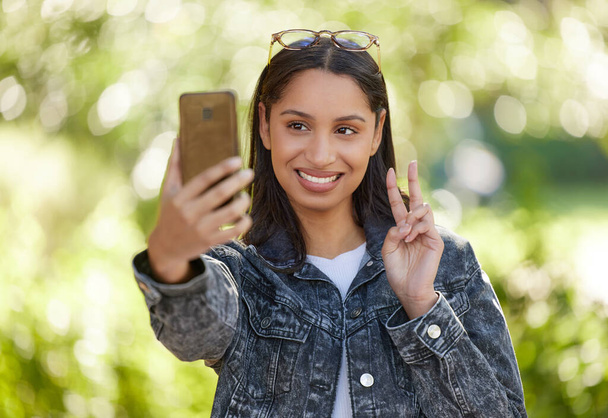 Peace and love. a beautiful young student using her phone while standing outside - Zdjęcie, obraz
