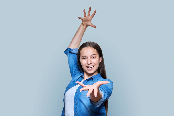 Emotional beautiful teenage girl in expression with arms raised open smile screaming wow, on light gray color studio background. Emotions expression joy happiness success dance concept - Foto, Imagen