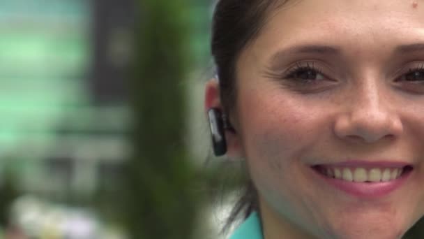 Geschäftsfrau mit Bluetooth-Gerät blickt lächelnd in die Kamera - Filmmaterial, Video