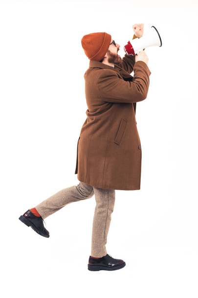 Full body shot of a stylish bearded man in a autumn coat using a loudspeaker on a white infinity background. High quality photo - Foto, immagini