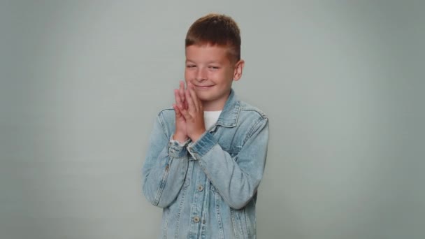 Sneaky cunning boy with tricky face gesticulating and scheming evil plan, thinking over devious villain idea, cunning cheats, jokes and pranks. Toddler teenager child on gray studio background alone - Záběry, video