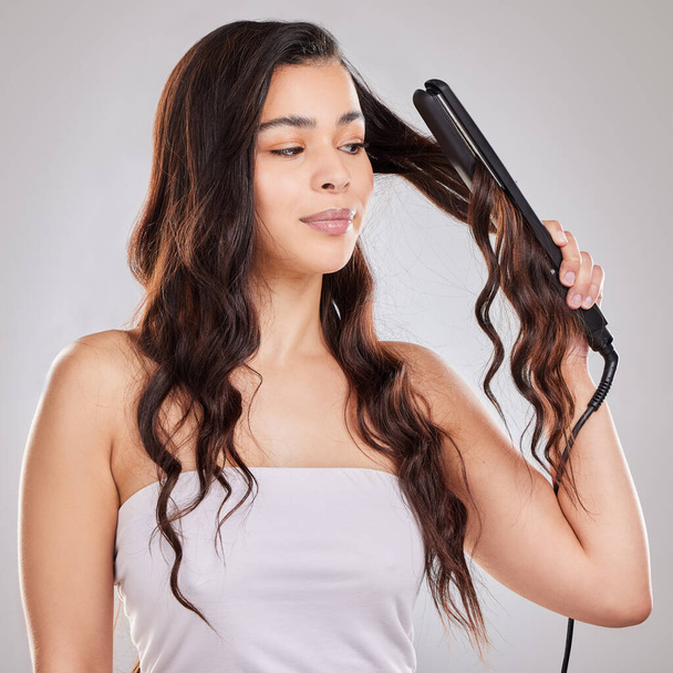 From curly, to straight. Studio shot of a beautiful young woman using a straightener on her hair - Fotoğraf, Görsel