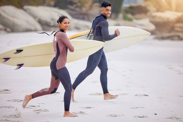Surfing is almost a way to fly. Portrait of a young couple running towards the sea with their surfboards - Foto, Imagen