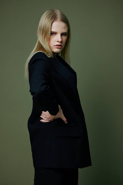 A professional blonde model holds her waist with both hands half-turned looks at the camera posing on a green background in the studio. High quality photo - Photo, Image