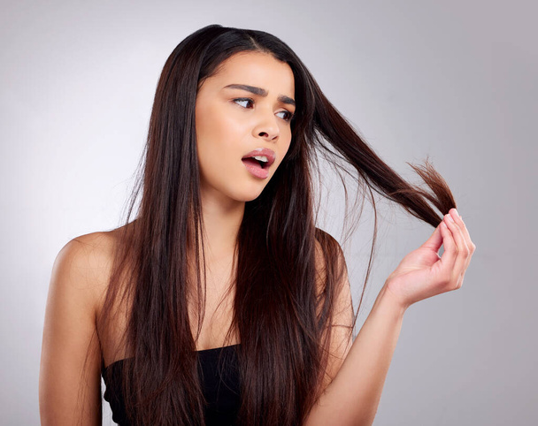 Split ends. Why now. Studio shot of an attractive young woman having a bad hair day against a grey background - 写真・画像