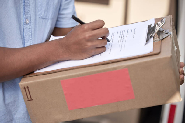 Taking care of logistics. Closeup shot of an unrecognisable delivery man using a clipboard while holding a box - Foto, Imagen
