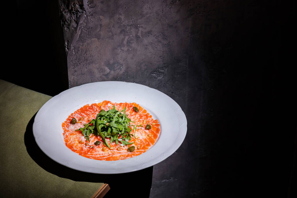 Salad with salmon, parmesan, arugula, chickpeas and seeds in a plate on the edge of the table against the background of a stone wall - Valokuva, kuva