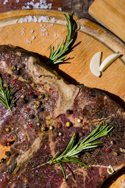 Grilled beef meat on the bone with cloves of garlic, rosemary, salt and peppercorns on a wooden board and wooden table. Vertical orientation - Zdjęcie, obraz
