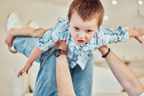 Adorable little caucasian boy lift into the air by his father so he can pretend to fly like a plane or superhero with arms out while relaxing at home. Loving dad playing and bonding with carefree kid. - Foto, immagini